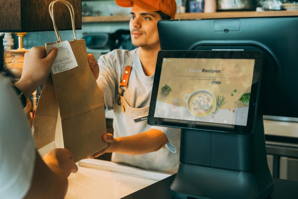 Customer receiving takeaway bag from waiter at counter with EPOS system - payment provider comparison business example