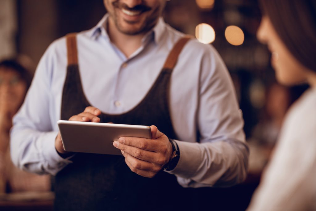 Supervisor providing EPOS training Ireland to waiter using tablet for POS system staff training in Irish restaurant