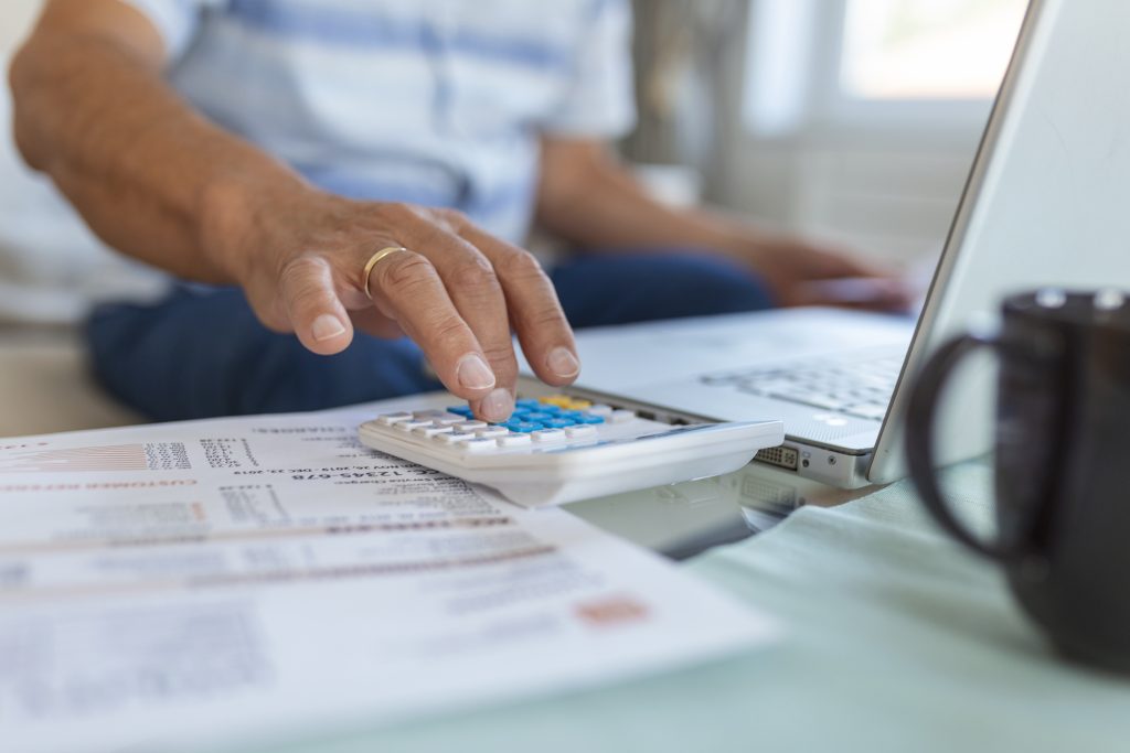Business owner using calculator to calculate payment processing tax deductions Ireland on laptop at desk
