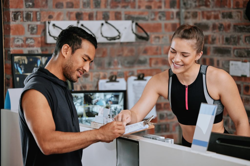 Gym payments Ireland – gym member talking with receptionist while reviewing a flyer at the front desk