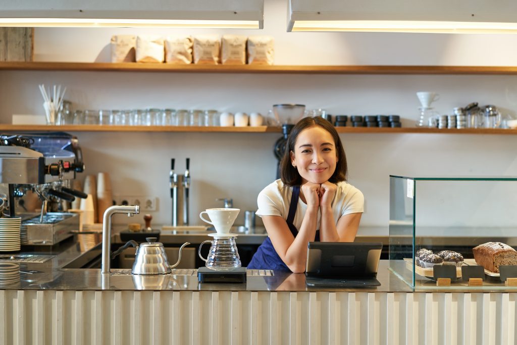 Female waiter at Irish coffee shop counter with tablet EPOS system for credit card processing Ireland reducing card processing fees Ireland
