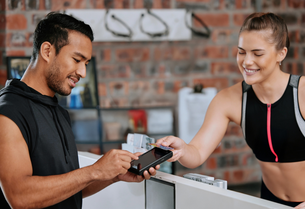 Customer making contactless payment at gym reception showing wellness payments Ireland with recurring billing and membership management