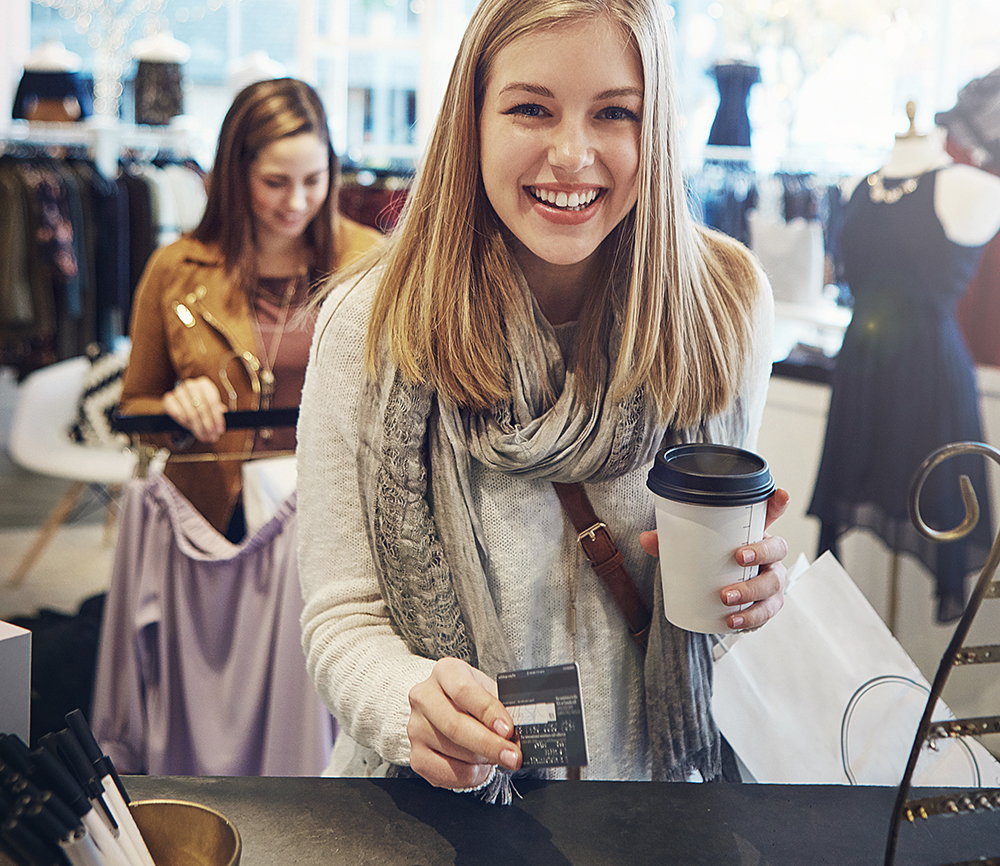 Happy woman making a contactless payment limit Ireland card transaction at a boutique retail store checkout